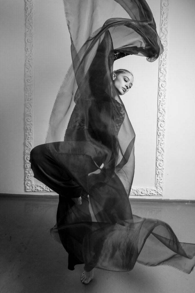 HOME Graceful contemporary dancer wearing flowing fabric in a black blouse and pants performing indoors.